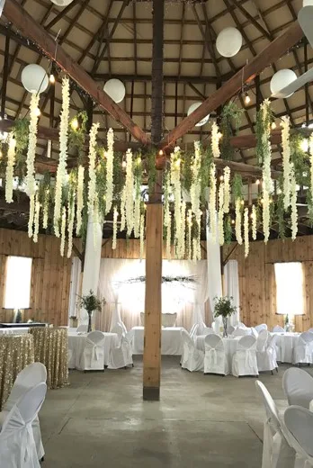Inside Heritage Hall set for a reception: the timber roof frame meets at a centre post above round tables, hung with white flowers and paper lanterns